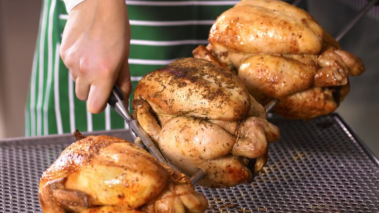 hand taking whole rotisserie chickens off spike