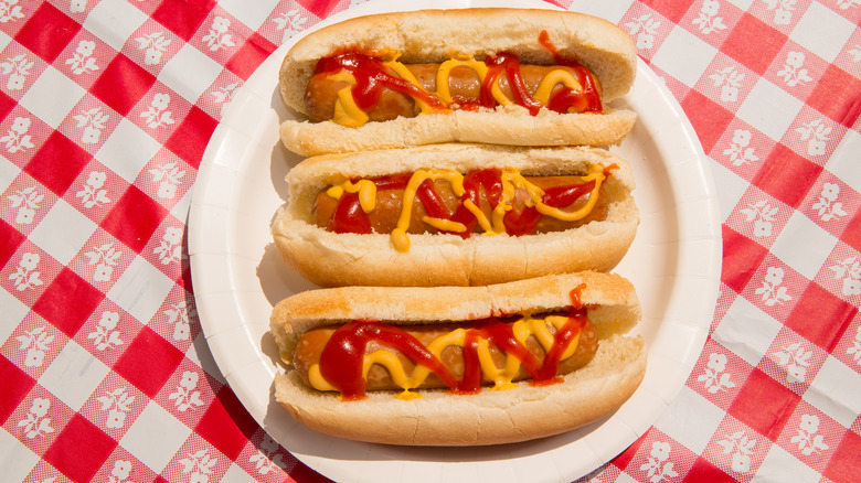 Three cooked hotdogs on buns on a paper plate on a table