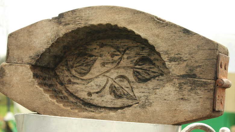 A vintage wooden butter mold with a carved leaf design