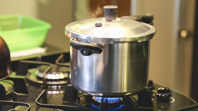 A pressure cooker on a gas stove with some steam rising from the lid