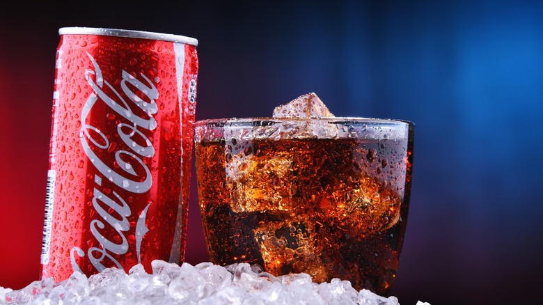 A glass and a can of Coca-Cola in ice.