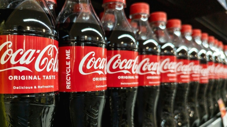 A row of Coca-Cola bottles on a supermarket shelf.