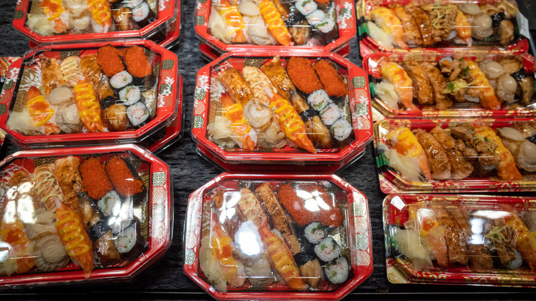 Takeout containers containing a variety of sushi rolls are lined up together