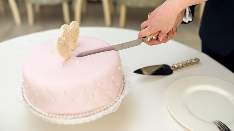 Two people holding a cake knife and cutting into a pink wedding cake