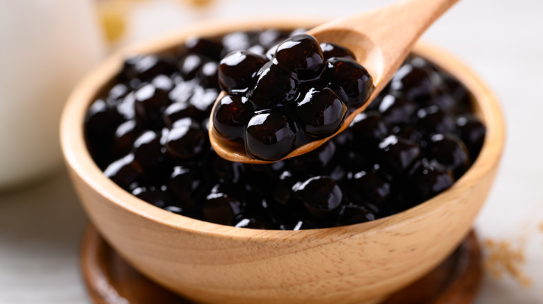 A wooden bowl full of black tapioca pearls and a wooden spoon scooping some up