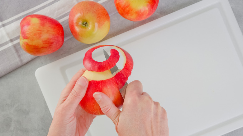 peeling red apples on white cutting board