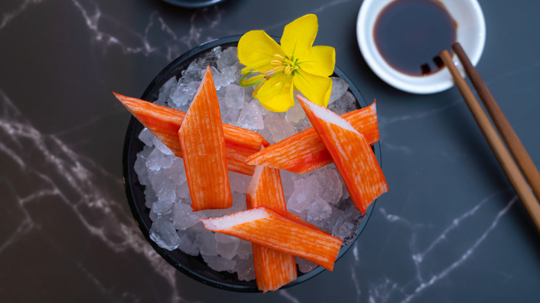 A bowl of imitation crab sticks on ice with a yellow flower garnish