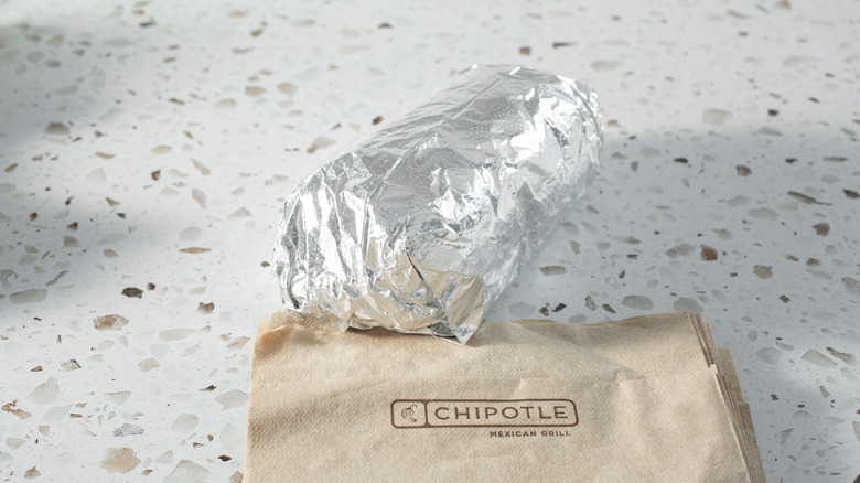 a chipotle burrito wrapped in aluminum foil with logo napkins