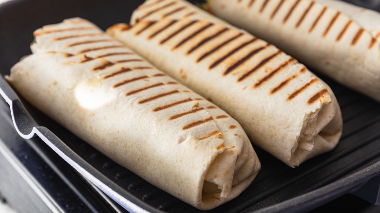 three burritos on a grill pan with grill marks on top