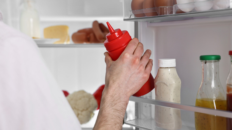 Man removing red plastic squeeze bottle of ketchup from fridge