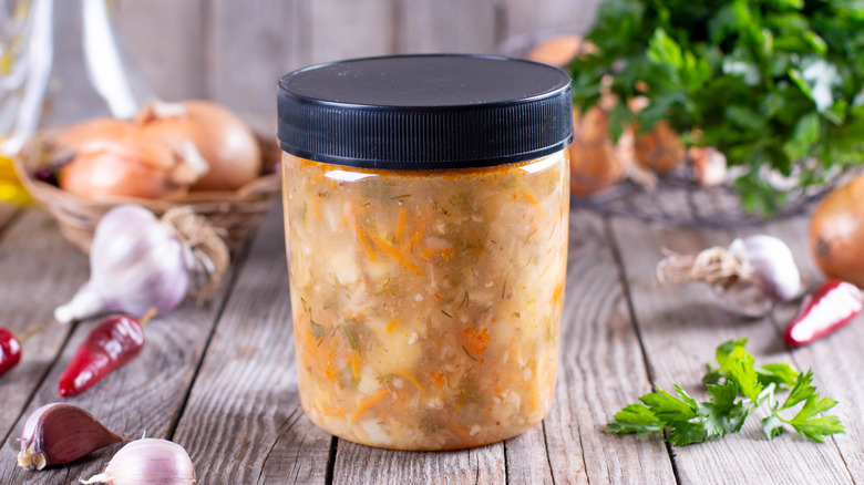 Container of frozen soup on wood with aromatics