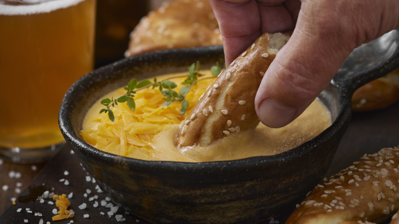 A hand dipping a pretzel bite into a bowl with beer cheese