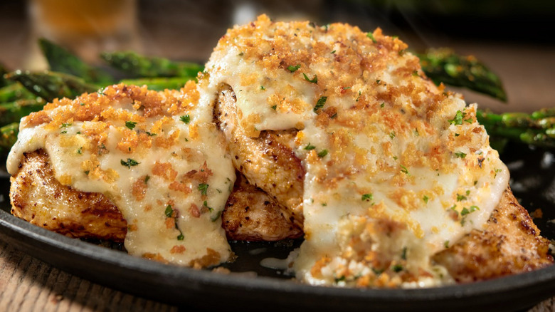 parmesan crusted chicken on a black plate with asparagus.