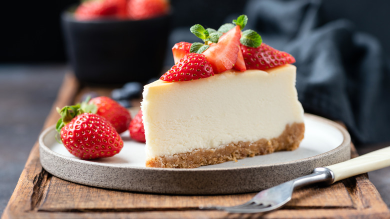 A slice of cheesecake topped with sliced strawberries on a wooden board