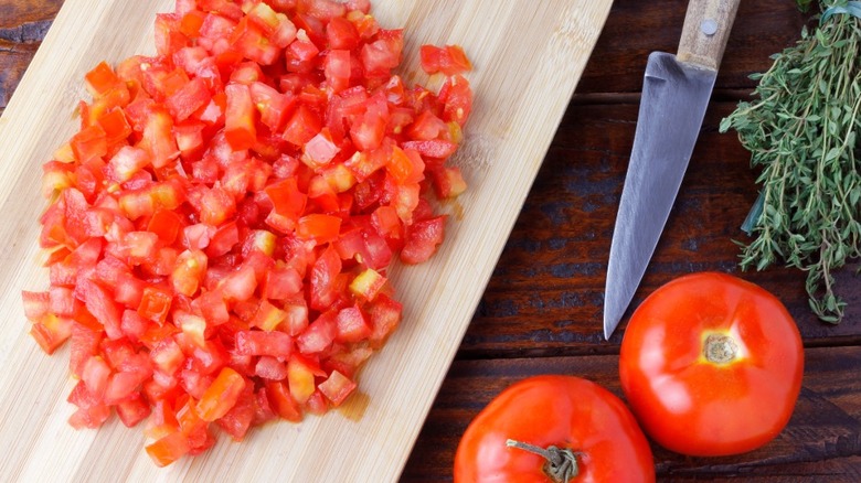 diced tomatoes on wooden cutting board near whole tomatoes and chopping knife