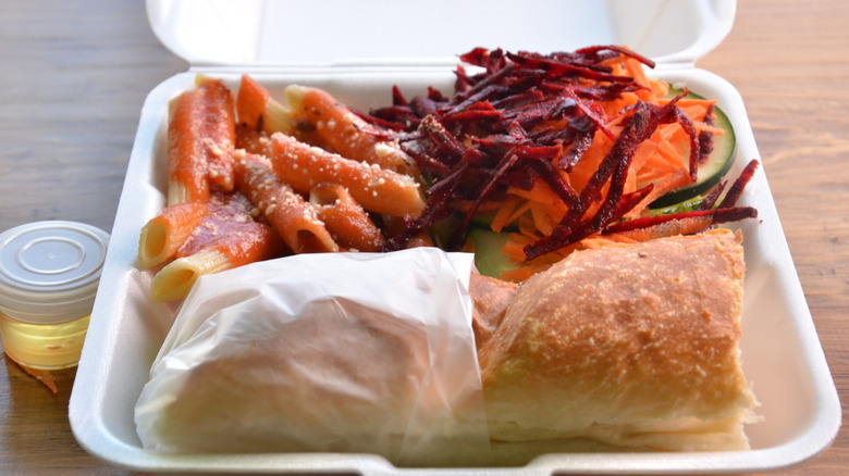 Styrofoam container containing salad, pasta and a sandwich.