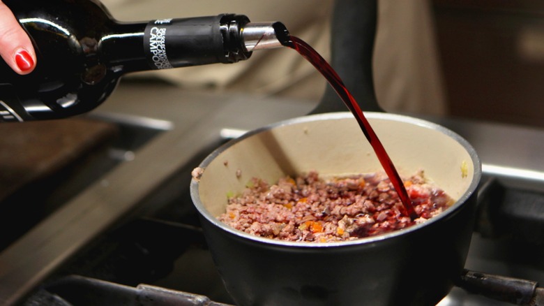 Woman pours red wine into pan on gas grill.