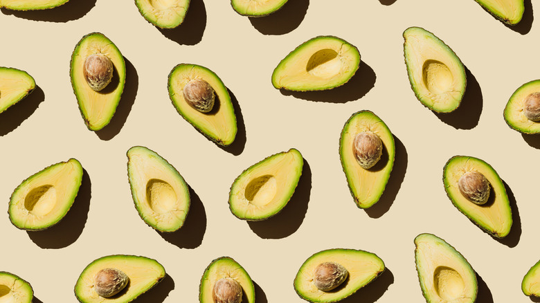 Avocados cut in half on a tan background