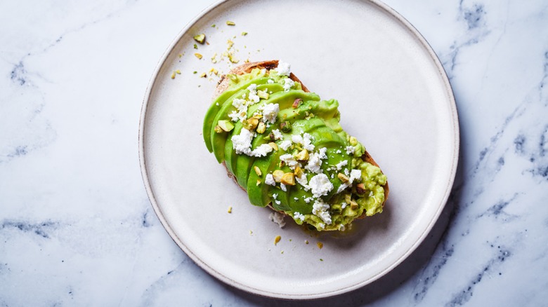 Sliced avocado on toast with cheese toppings on a white plate