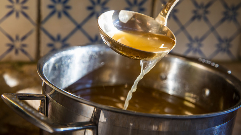 A ladle scooping chicken stock from a pot