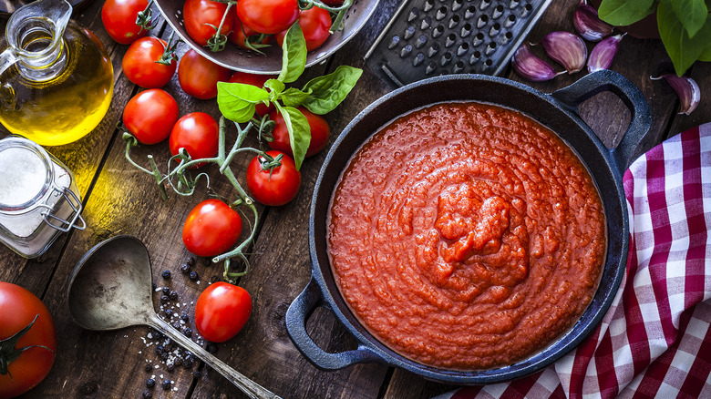 Black pot of marinara sauce next to tomatoes, basil, and other ingredients