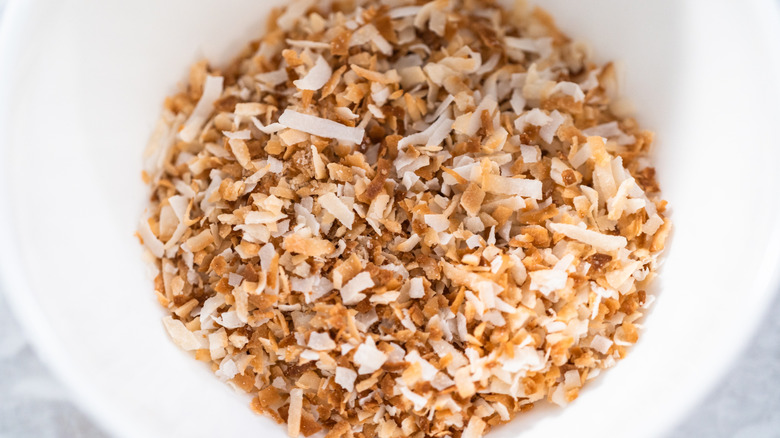 A pile of toasted coconut flakes sitting in a white bowl.