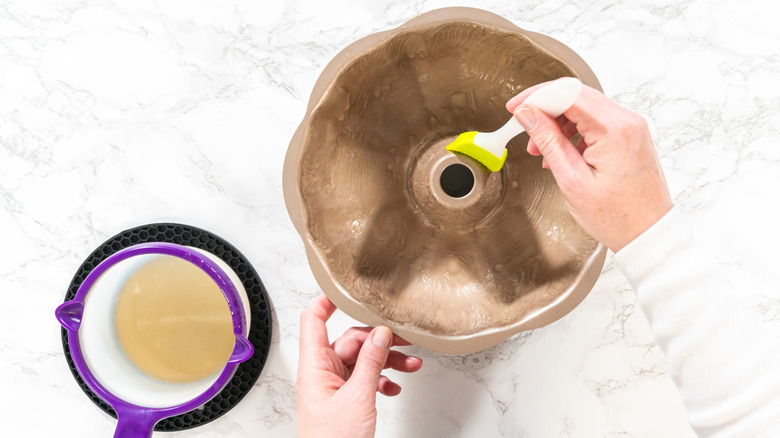 A baker greases a bundt pan with melted butter