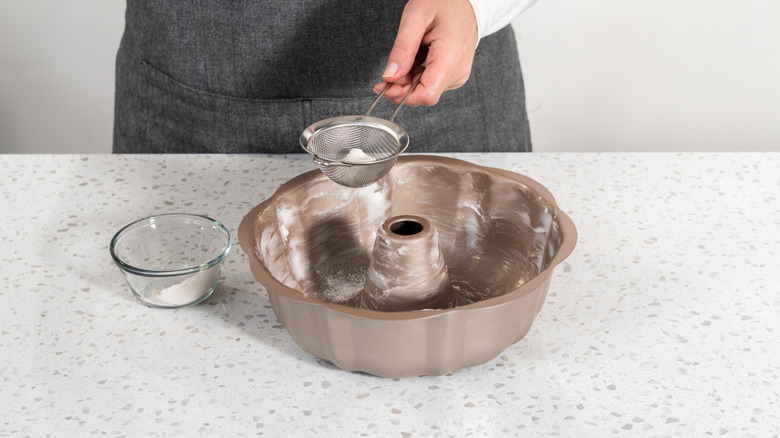 A baker dusts a greased bundt pan with sugar