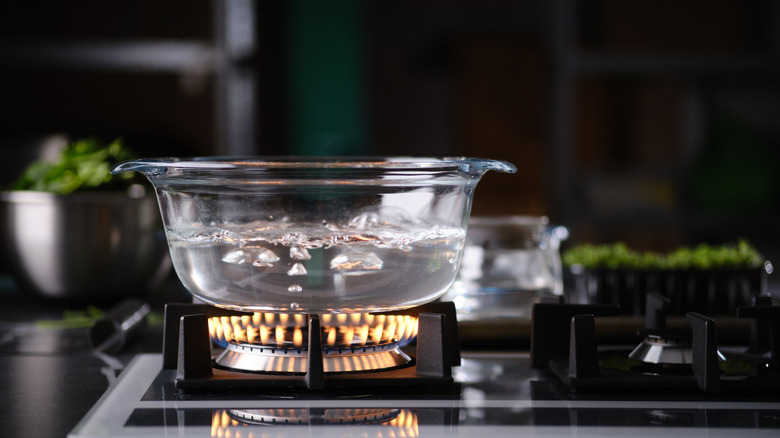 A glass dish with water inside boiling on a gas stovetop