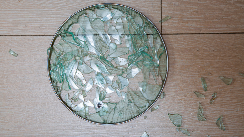 A shattered glass pot lid on a wooden floor