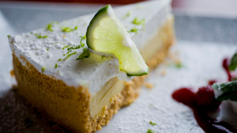 A close up of a slice of key lime pie with a lime wedge on top