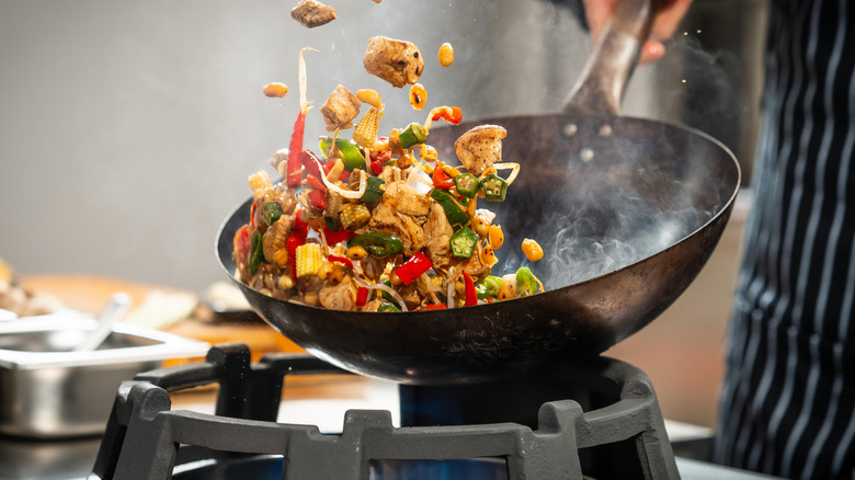 Wok over fire with stir fry being tossed.