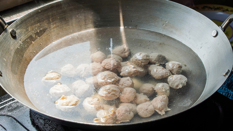 Stainless steel wok with simmering meatballs.