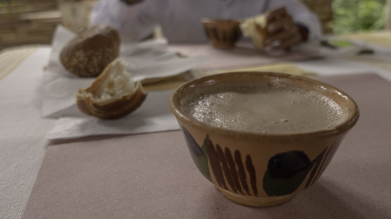 A cup of Mexican hot chocolate is shown with a piece of bread on a table