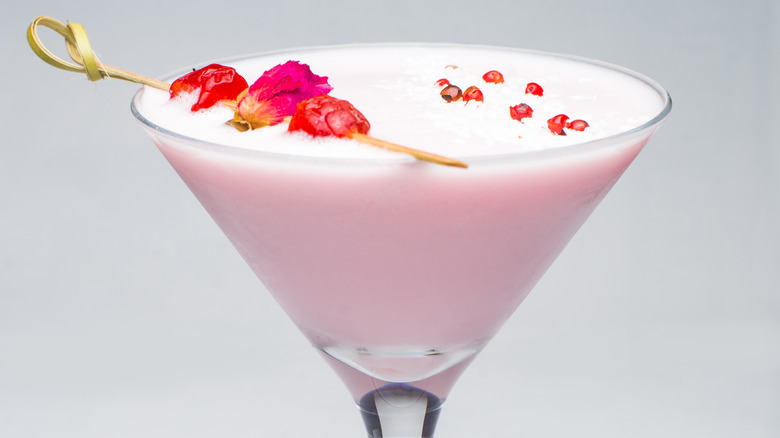 Pink squirrel cocktail in a martini glass garnished with edible flowers and petals.