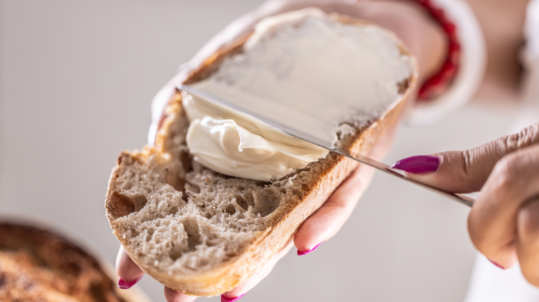 Person spreading cream cheese on bread.