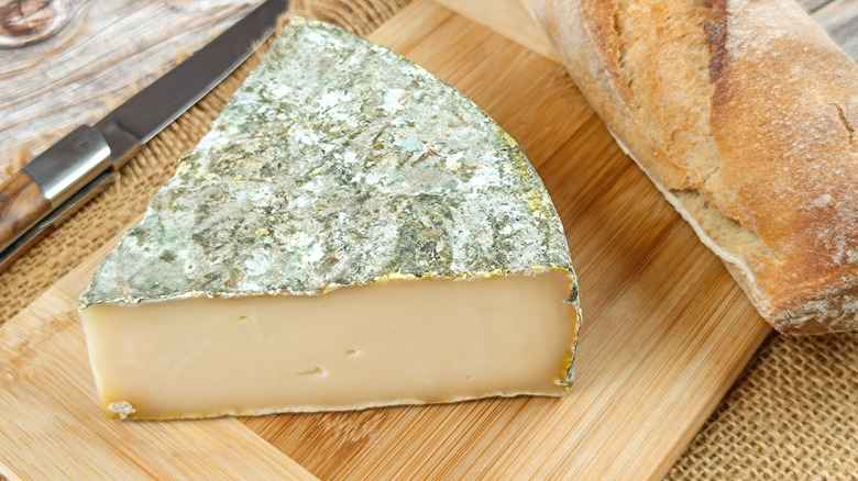 A wedge of Saint-Nectaire cheese on a cutting board.