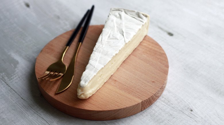 A piece of brie sitting on a wooden tray.