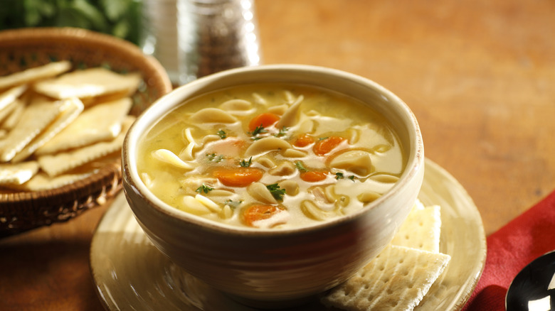 Chicken noodle soup in a bowl on a plate with crackers