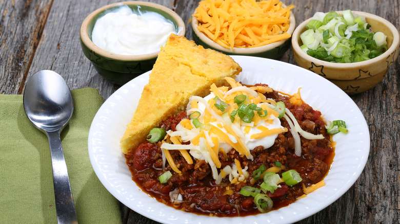 Chili and cornbread topped with cheese, sour cream, and green onion in a bowl