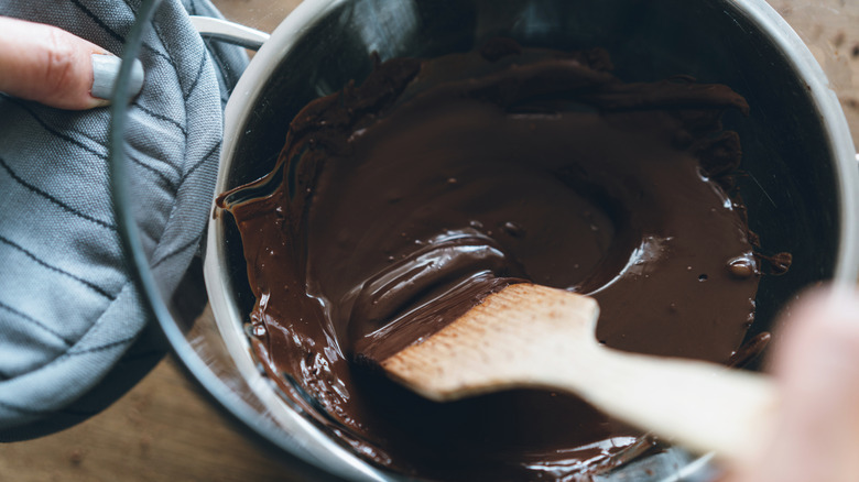 A wooden tool mixing a bowl of melting chocolate on top of a hot pot.