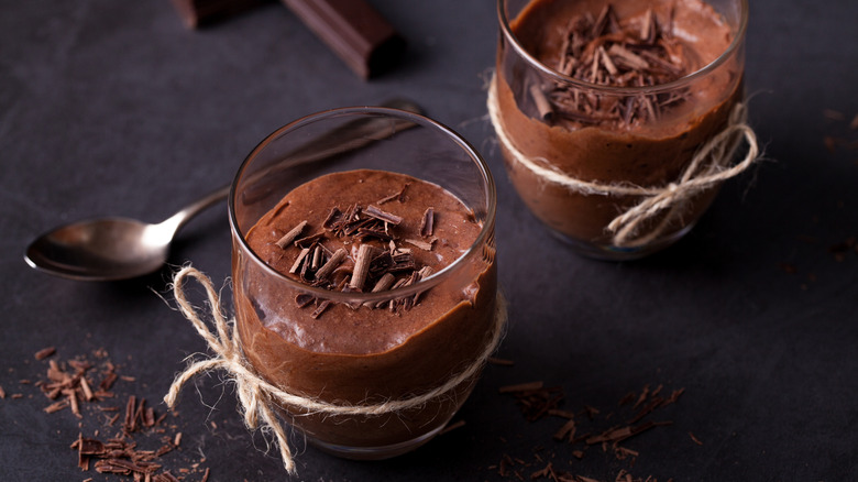 Two chocolate mousse cups on a black surface.