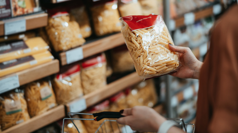 Woman holds bag of dry pasta in pasta aisle at grocery store