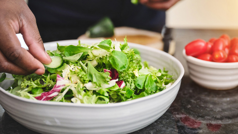 a man's hand putting a piece of cucumber onto a green salad