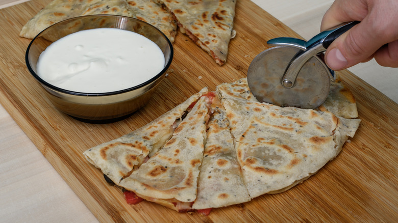 a pizza cutter being used to slice up a quesadilla