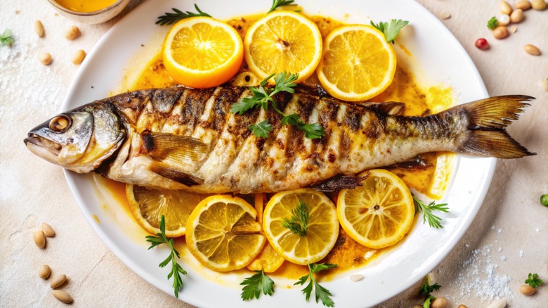 A grilled fish surrounded by lemon slices on a plate