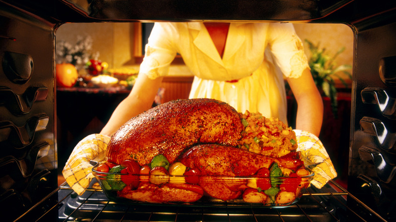 Person in 1950s clothing pulling turkey out of oven