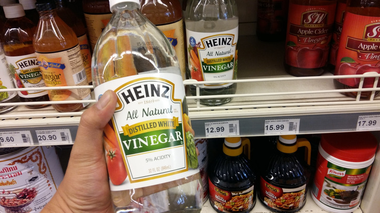 a man's hand holding a bottle of Heinz distilled white vinegar, store shelves