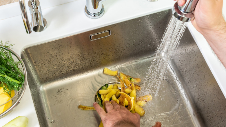 Someone pushing potato scraps down the garbage disposal