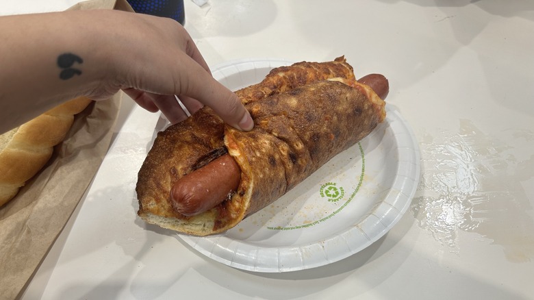 hand holding Costco hot dog wrapped in cheese pizza slice